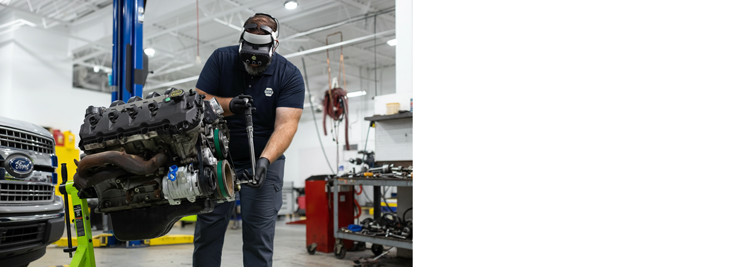 Automotive technician wearing a virtual reality headset while using a tool on an engine in a workshop.