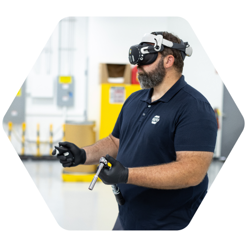 Automotive technician wearing a virtual reality headset while using a tool on an engine in a workshop.